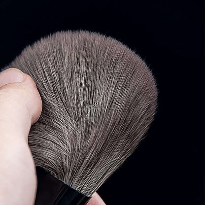 Makeup Brushes Set featuring dense, soft, synthetic grey bristles with a black handle held against a black background.