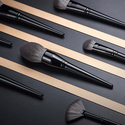 Makeup Brushes Set with black lacquered wooden handles and soft synthetic gray bristles in various shapes and sizes on a dark background.