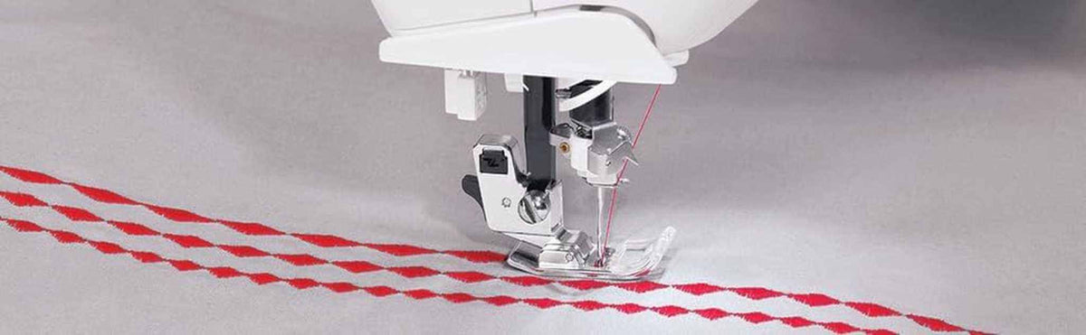 4723 Universal Regular Point Sewing Machine Needles stitching red zigzag pattern on light grey fabric with a silver sewing machine foot