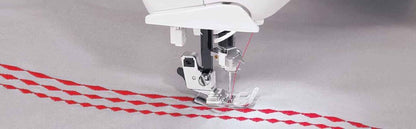 4723 Universal Regular Point Sewing Machine Needles stitching red zigzag pattern on light grey fabric with a silver sewing machine foot