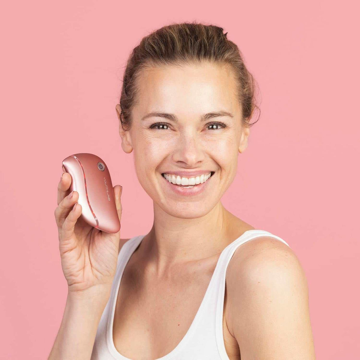 Heated Gua Sha Tool in rose gold with ergonomic curved design held by smiling woman with light skin and pulled-back hair